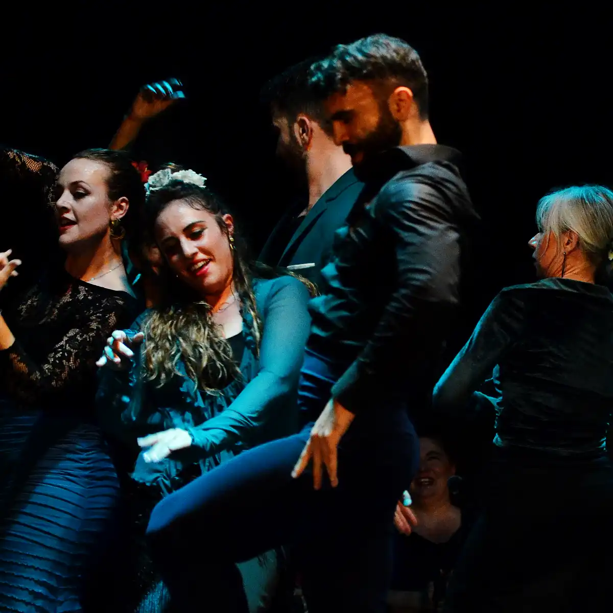 Un gruppo di ballerini di flamenco sul palco, illuminati da luci di scena.