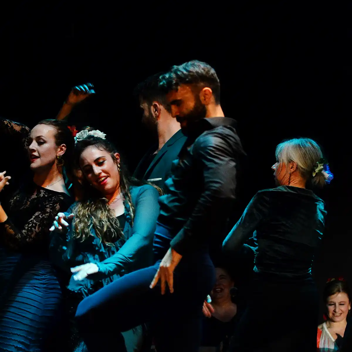 Un gruppo di ballerini di flamenco sul palco, illuminati da luci di scena.