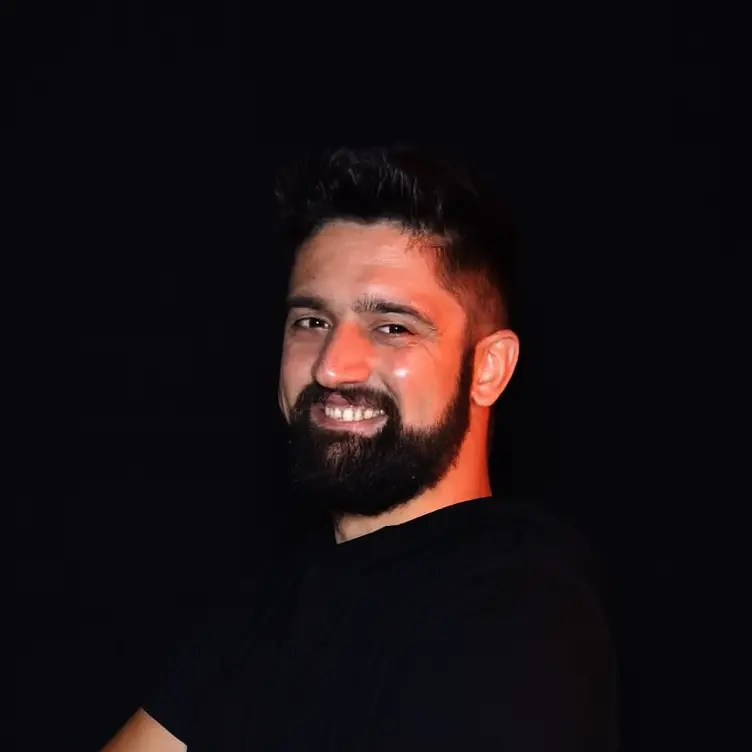 Ritratto sorridente di Gio Juan, insegnante di salsa cubana presso Il Mosaico Danza a Milano, con maglietta nera e sfondo scuro brandizzato