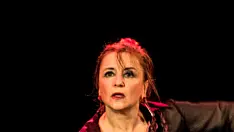 Sabina Todaro esegue una potente performance di flamenco, indossando un abito tradizionale nero con accenti rossi e viola. Le sue braccia sono sollevate in una posa espressiva e il suo volto intenso trasmette tutta la passione e la drammaticità della danza. Lo sfondo scuro mette in risalto la sua figura e l'energia del momento.